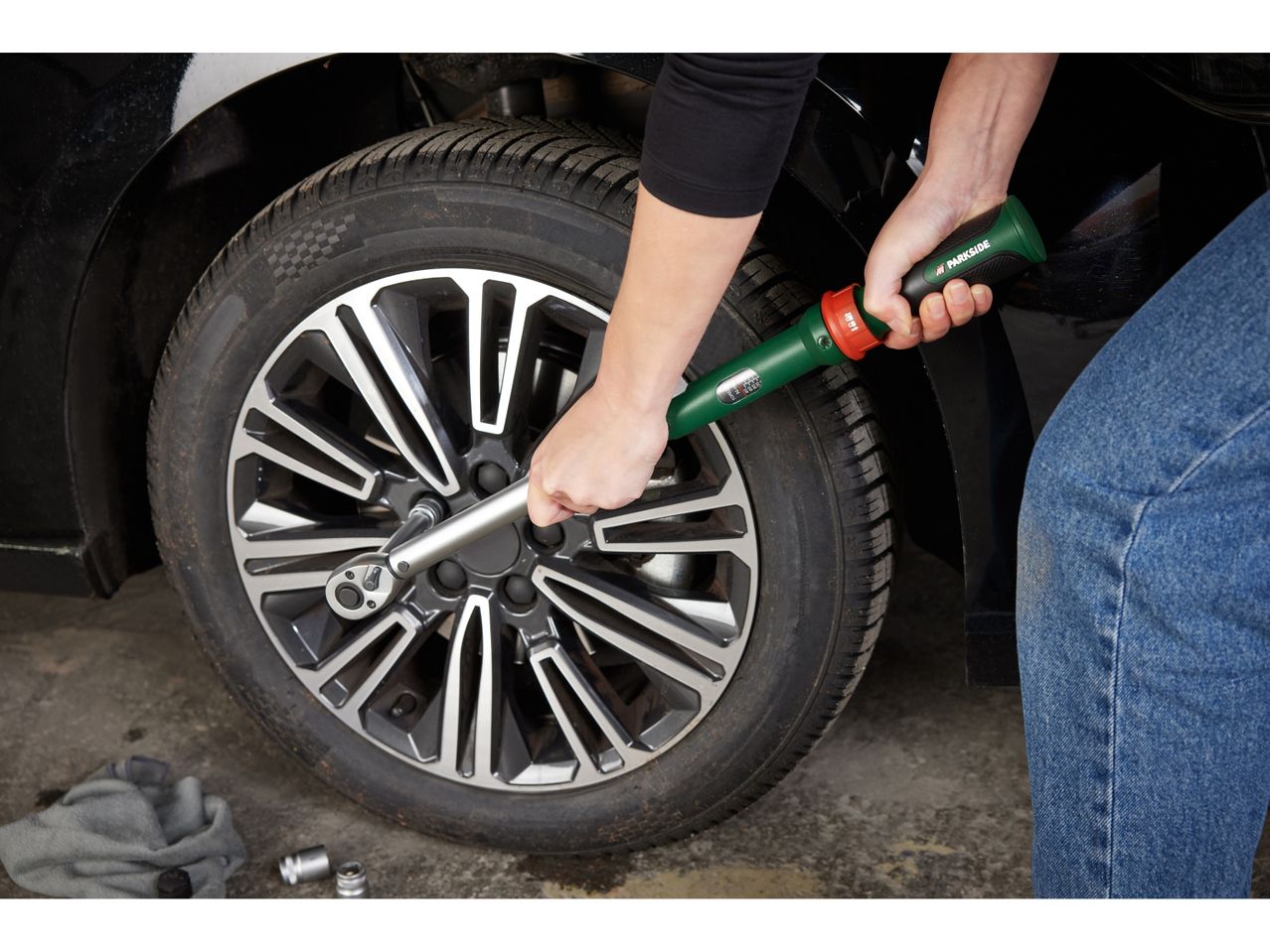 A person uses a Parkside torque wrench to tighten a wheel nut on a car.