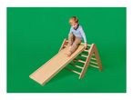 A young boy playing on a wooden indoor slide and climbing frame against a green background.