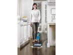A woman uses a Bissell Vacuum-Mop to clean up a spill on a hardwood floor in a kitchen.