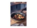 Frying pan with bacon-wrapped chicken and sage on a wooden board in a kitchen.