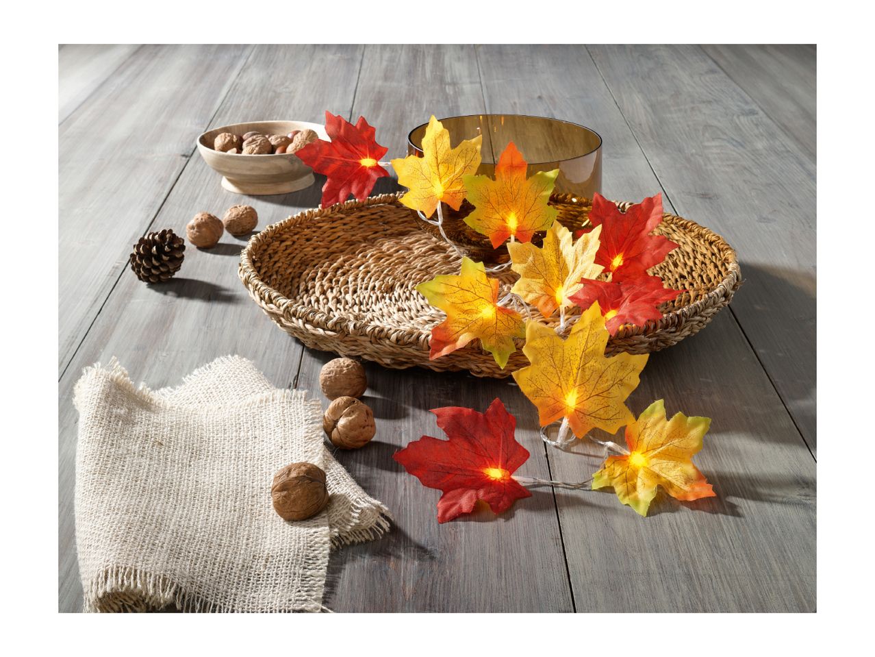 Autumnal decor with illuminated maple leaf garland, walnuts, pinecone, and a woven basket.