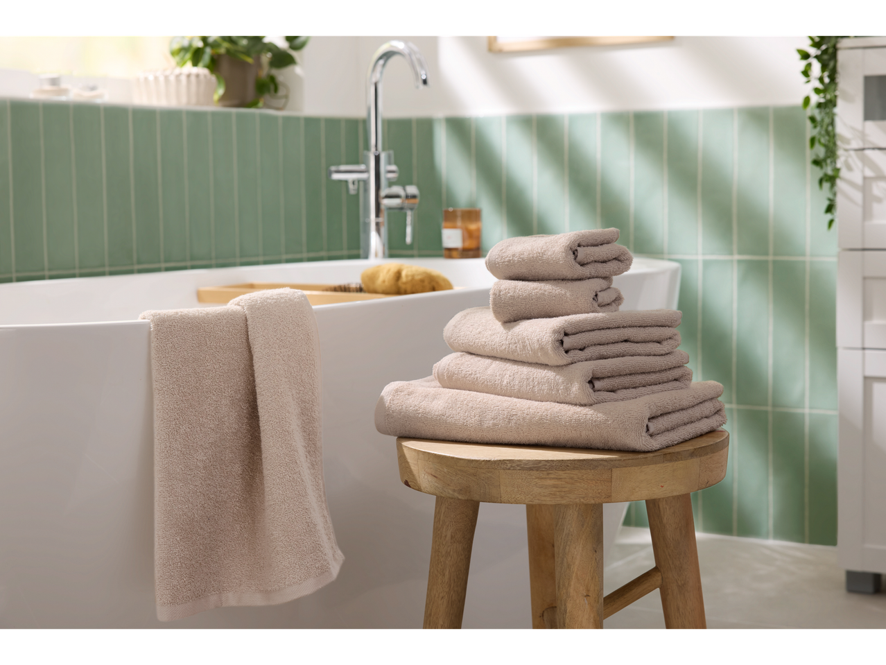 Sukrauti smėlio spalvos rankšluosčiai ant medinės taburetės šalia vonios moderniame vonios kambaryje.