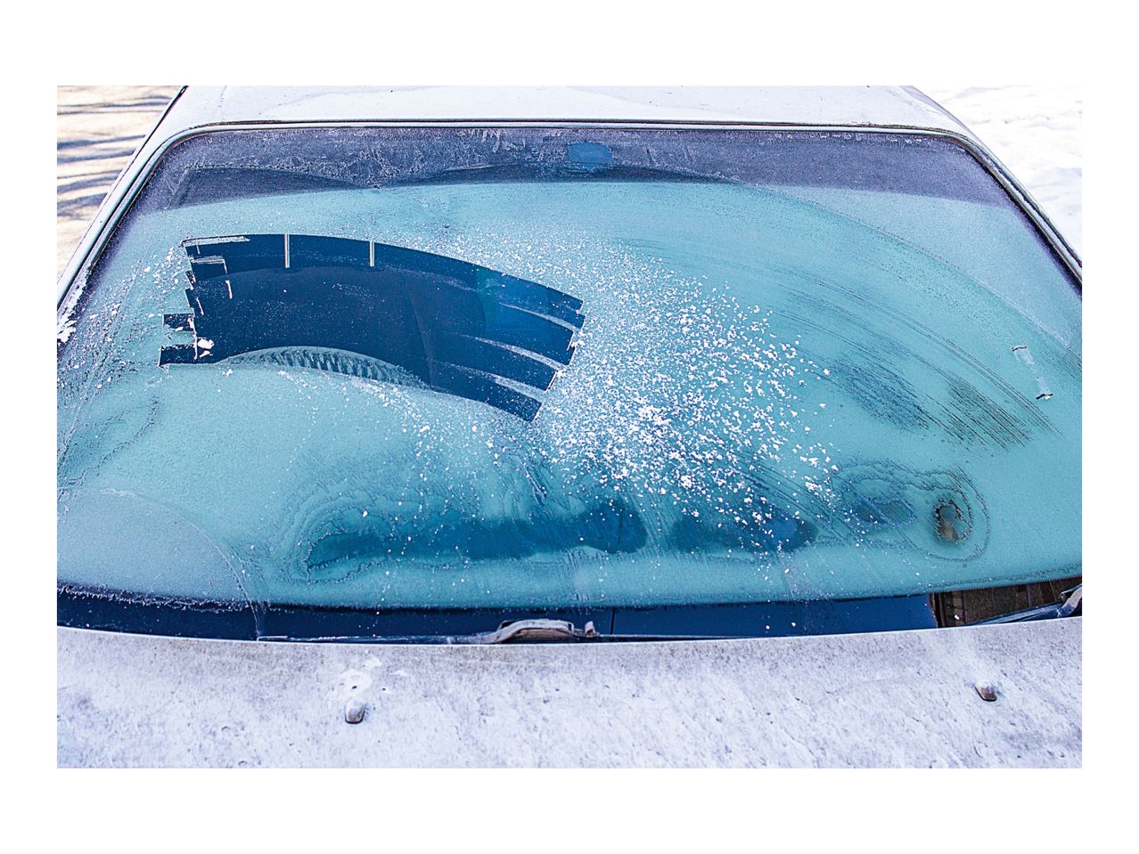 A car windshield covered in frost with a wiper clearing a section.