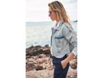 Donna in giacca di jeans, pantaloni blu e occhiali da sole sulla spiaggia.