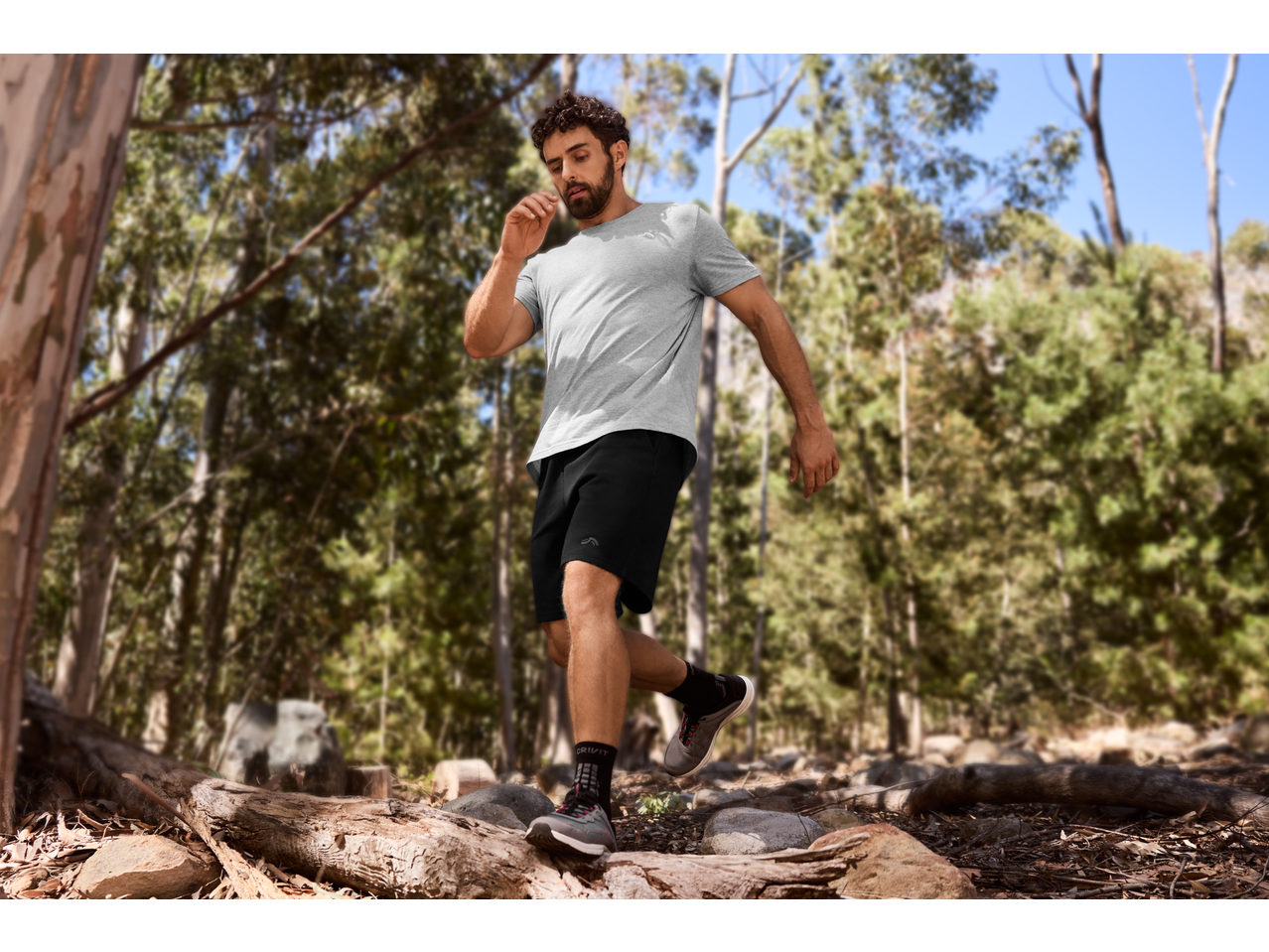 Homem com t-shirt CRIVIT e calções pretos a caminhar numa floresta.