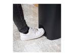 A person's foot in a white sneaker pressing the pedal of a black pedal bin.