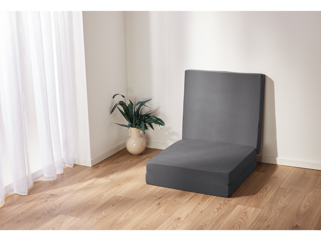 Grey foldable mattress on a light wood floor.