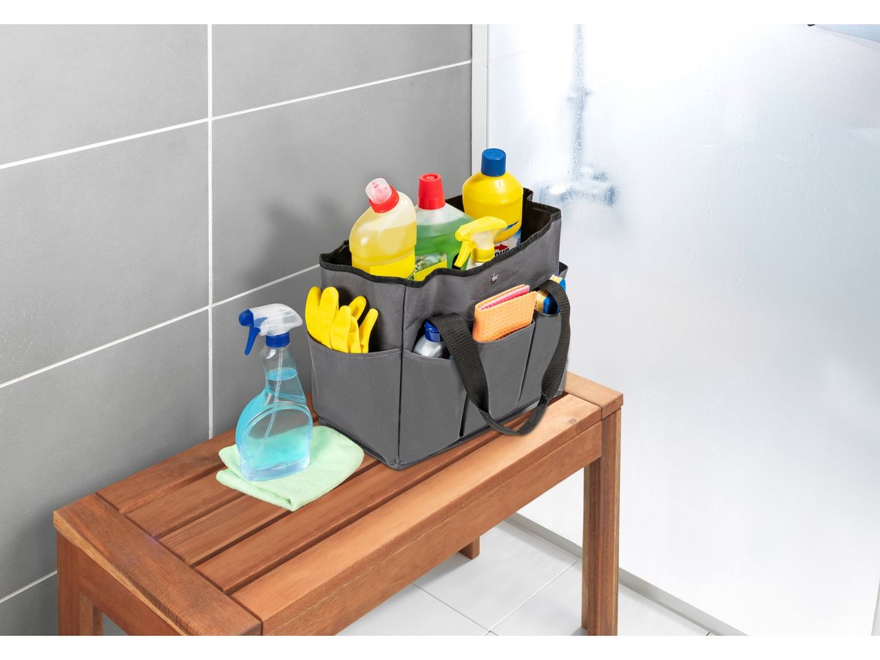 A gray cleaning caddy sits on a wooden bench, filled with cleaning supplies.