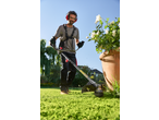 Man using a grass trimmer in a garden, wearing ear protection and safety glasses.