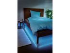 A wooden bed with blue striped bedding and blue under-bed lighting in a bedroom.