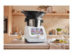 A Monsieur Cuisine Smart food processor on a kitchen counter with a meal and drinks.