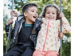 Two happy children in rain jackets and overalls on a swing.