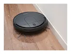 A black robotic vacuum cleaner on a wooden floor, next to a white wall.