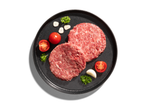 Két nyers hamburgerpogácsa egy sötét tányéron paradicsommal, fokhagymával és petrezselyemmel.