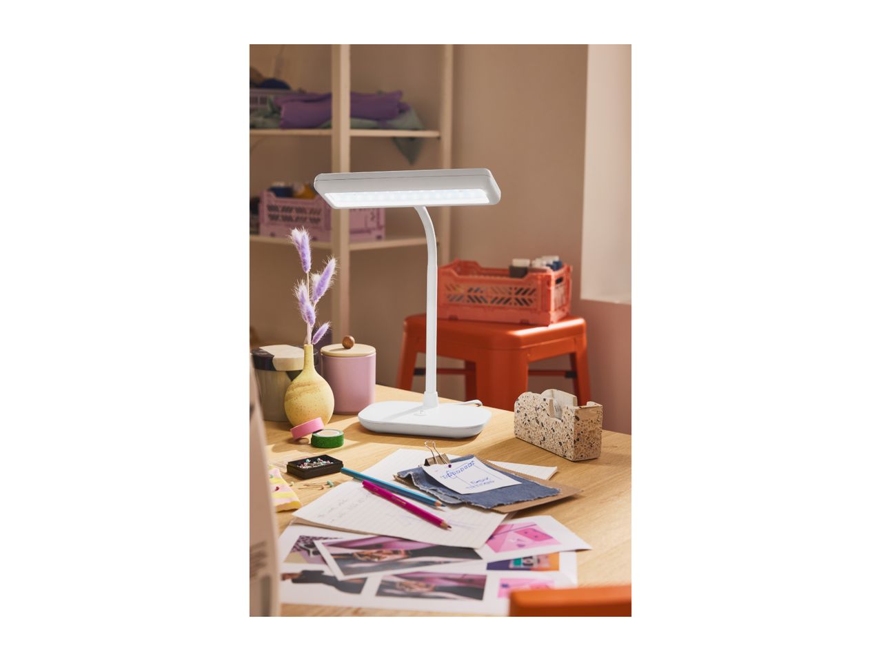 A white desk lamp illuminates a wooden desk with craft supplies and papers.
