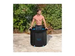 Man in a black portable ice bath on a patio with green foliage in the background.