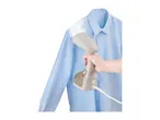 A hand holding a handheld garment steamer to steam a light blue shirt.