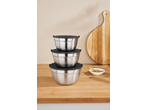 Stacked stainless steel mixing bowls with black lids on a wooden counter with a cutting board.