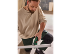 A man cutting a white pipe with a green pipe cutter.