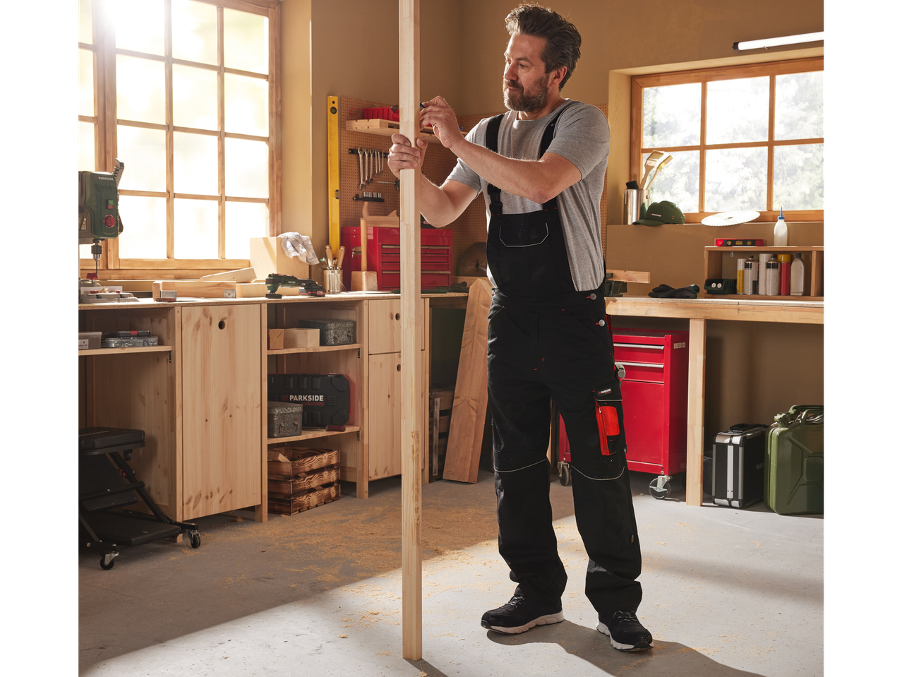 Man in Parkside overalls marking wood in a workshop.