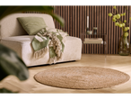 Beige sofa with green cushion and blanket, round jute rug on wooden floor, wood panel wall.