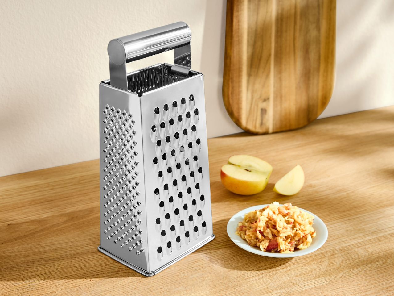 Stainless steel box grater with grated apple on a plate and apple slices