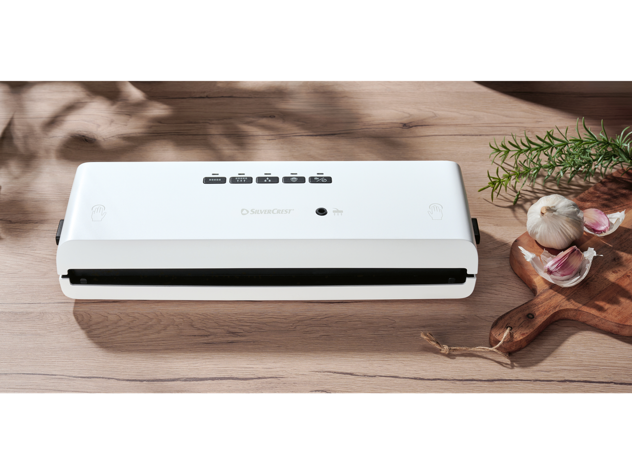 Silvercrest vakuum mašina na drvenom stolu sa belim lukom i ruzmarinom.