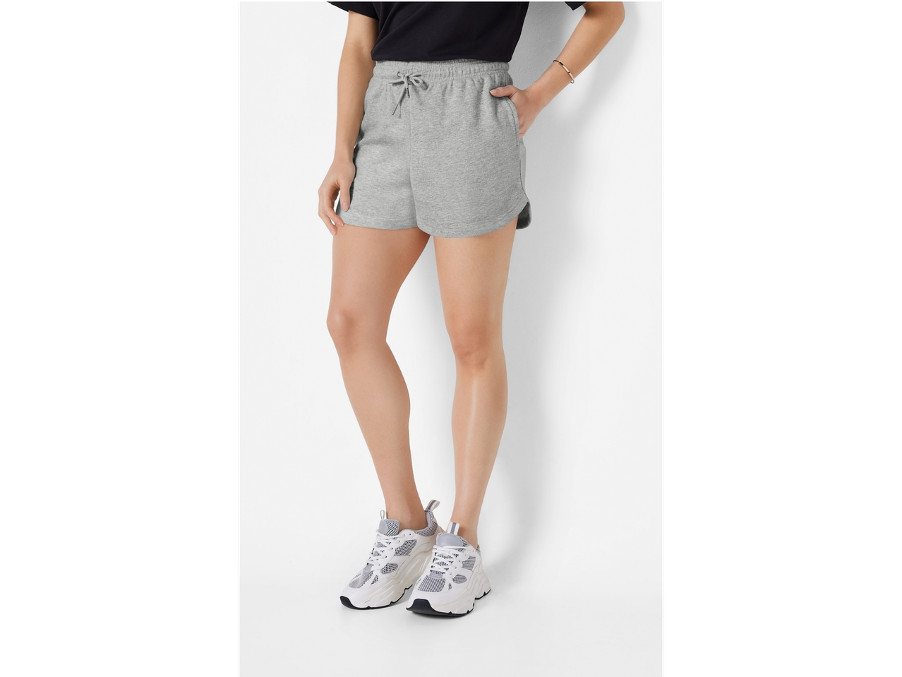 Femeie purtând pantaloni scurți sport gri și adidași albi.