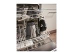 Open dishwasher with a blender, colander, and other kitchen items inside.