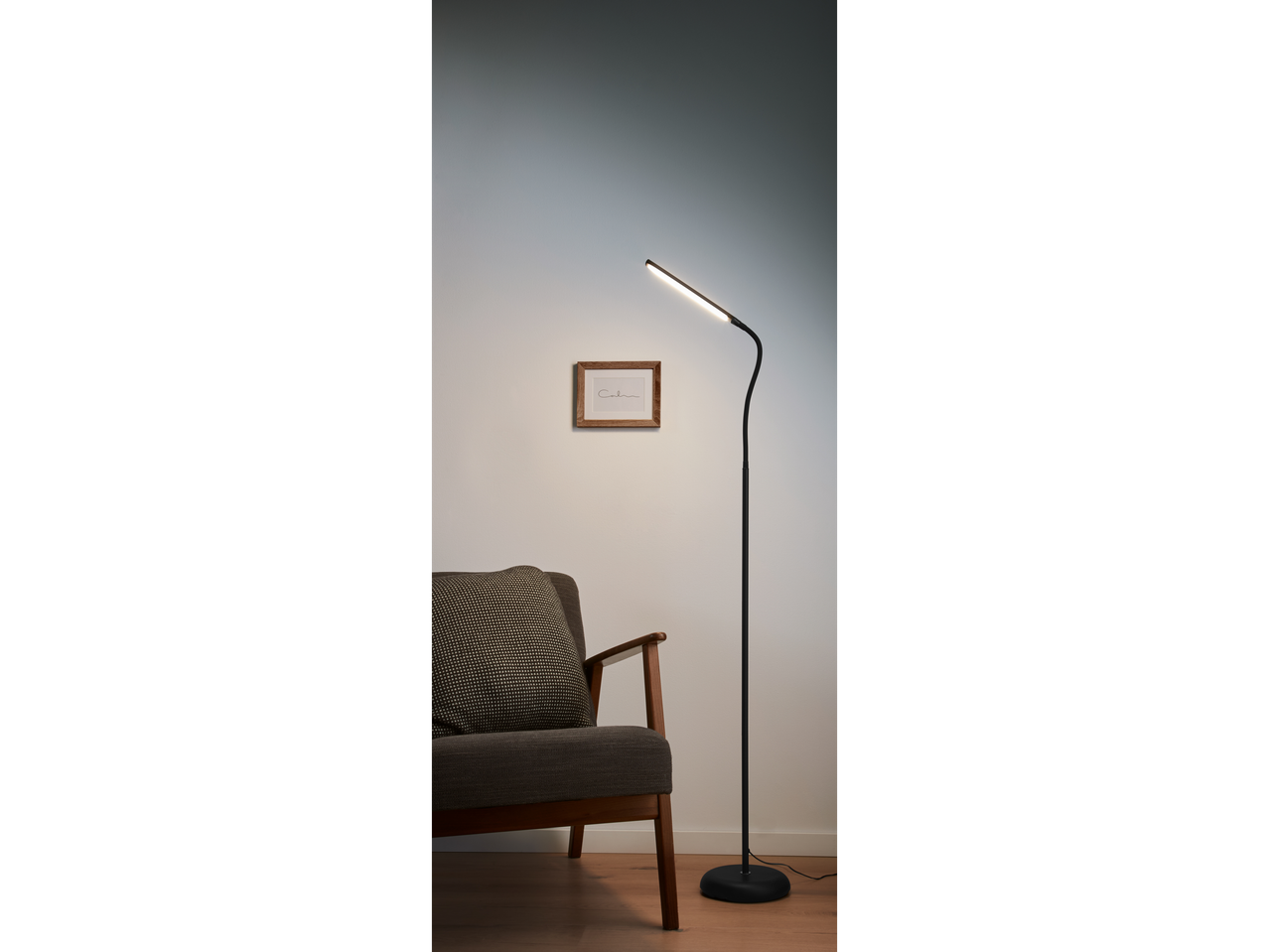 O lampă elegantă de podea LED neagră luminează un fotoliu confortabil într-o cameră minimalistă.