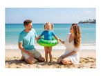 Family on a beach with a child wearing a blue swimsuit and a green inflatable swimming ring.