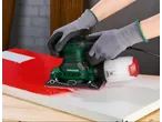 Hands in gloves using a PARKSIDE orbital sander on a red and white surface.