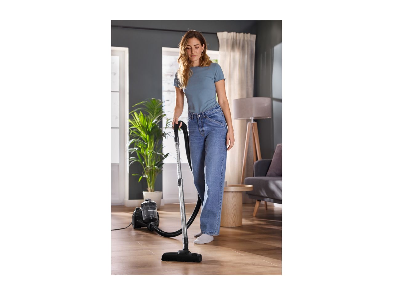 Woman vacuuming a wooden floor with a black cylinder vacuum cleaner.