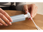 Mãos montando uma persiana de rolo com cordão branco em uma mesa de madeira.