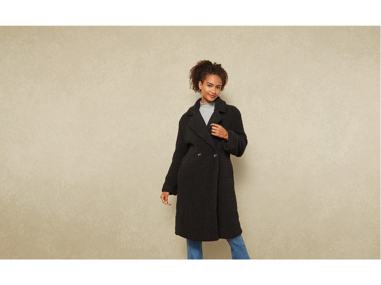 Donna in cappotto nero effetto Teddy, dolcevita grigio e jeans blu.