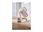 White electric kettle pouring hot water into a mug on a wooden countertop.