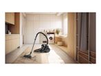 A black canister vacuum cleaner cleaning a rug in a modern laundry room.