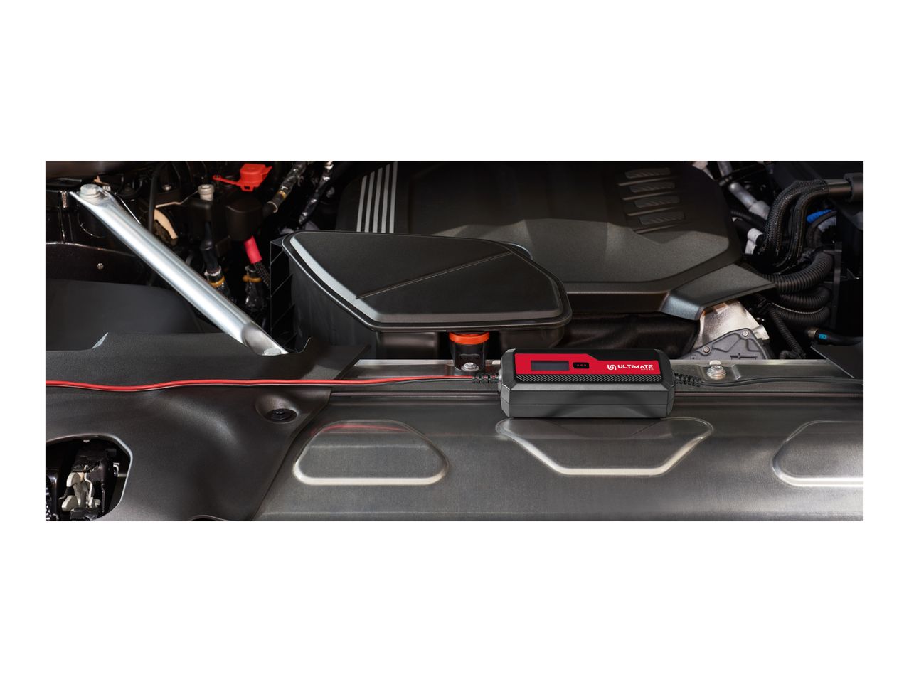A black and red Ultimate Speed battery charger connected to a car engine.