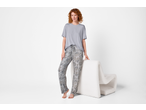 Woman in grey t-shirt and patterned pajama pants, leaning on a white chair.