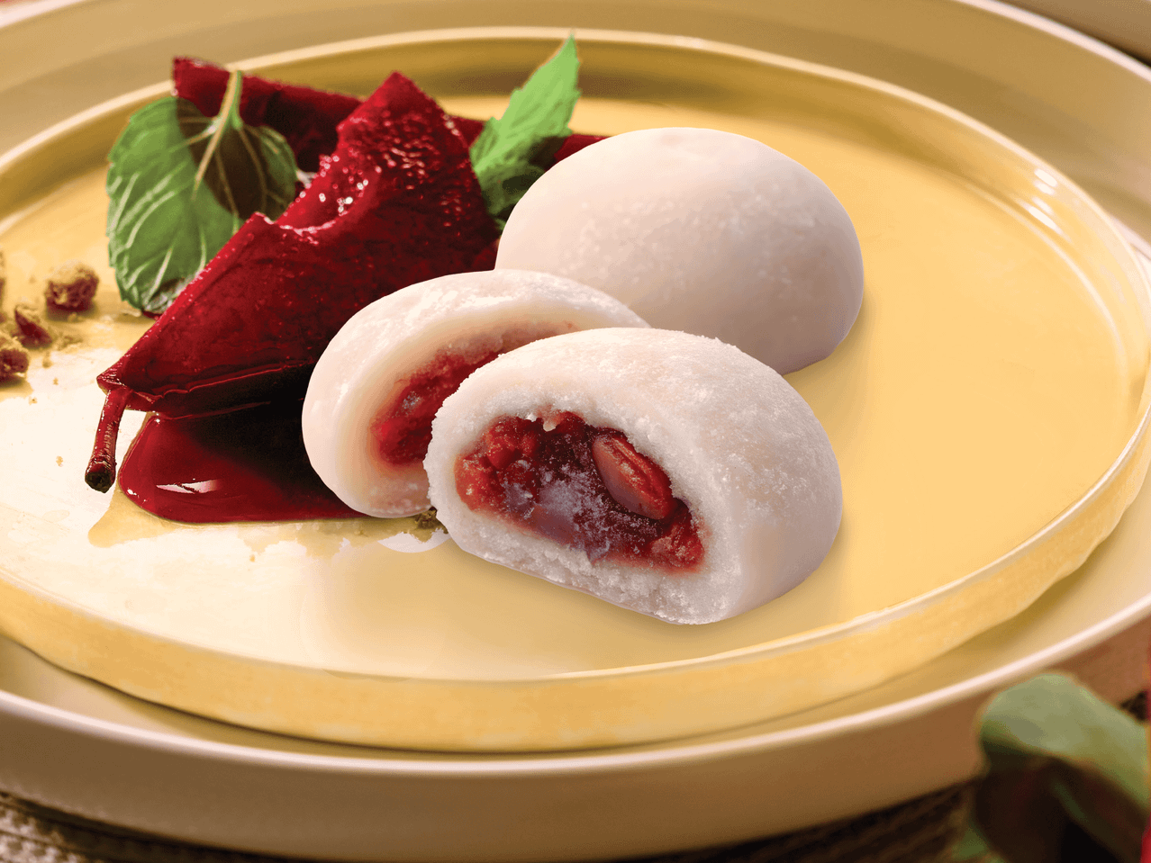 Mochi mit roter Bohnenfüllung, garniert mit Minze und roter Soße auf einem gelben Teller.