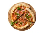 Pizza with ham, pesto, and basil on a wooden board, with two slices cut out.