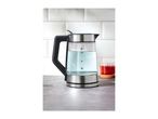 Glass kettle with water on a kitchen counter next to a glass of red tea.