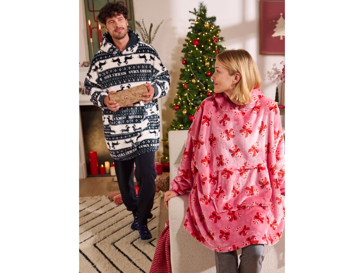 Man and woman in festive oversized hoodies, man holding a Christmas gift.