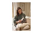 A woman sitting on a sofa and grooming a grey cat with a white pet brush.