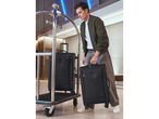 Man in a hotel lobby placing a black suitcase on a luggage cart.