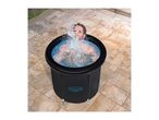 Man in a black portable ice bath, splashing water, on a tiled patio.