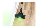 Cordless vacuum cleaner head with green LED lights illuminating dirt on a wooden floor.