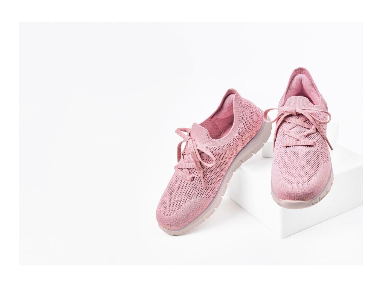 Pair of pink knitted sneakers with laces on white display blocks