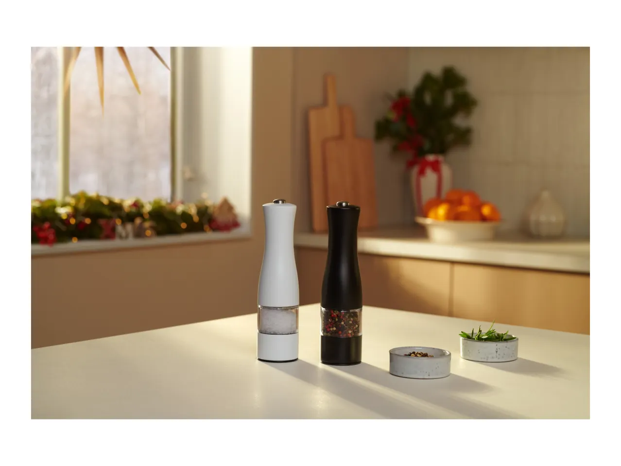 A white salt mill and a black pepper mill on a kitchen counter with festive decor.