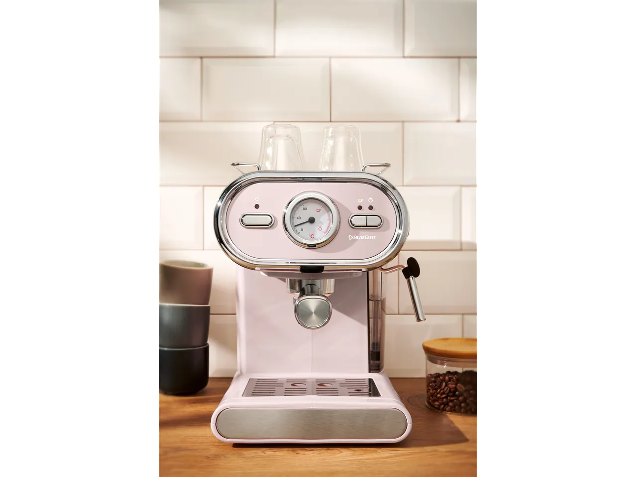 Pink SilverCrest espresso machine on a kitchen counter with cups and coffee beans.